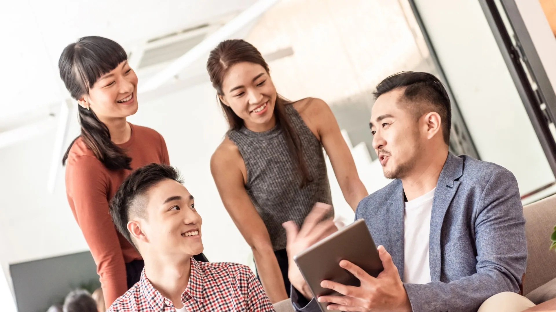 A next-generation team collaborating around a tablet in a bright modern workplace — FutureX Next-Gen Leadership for the AI Workplace