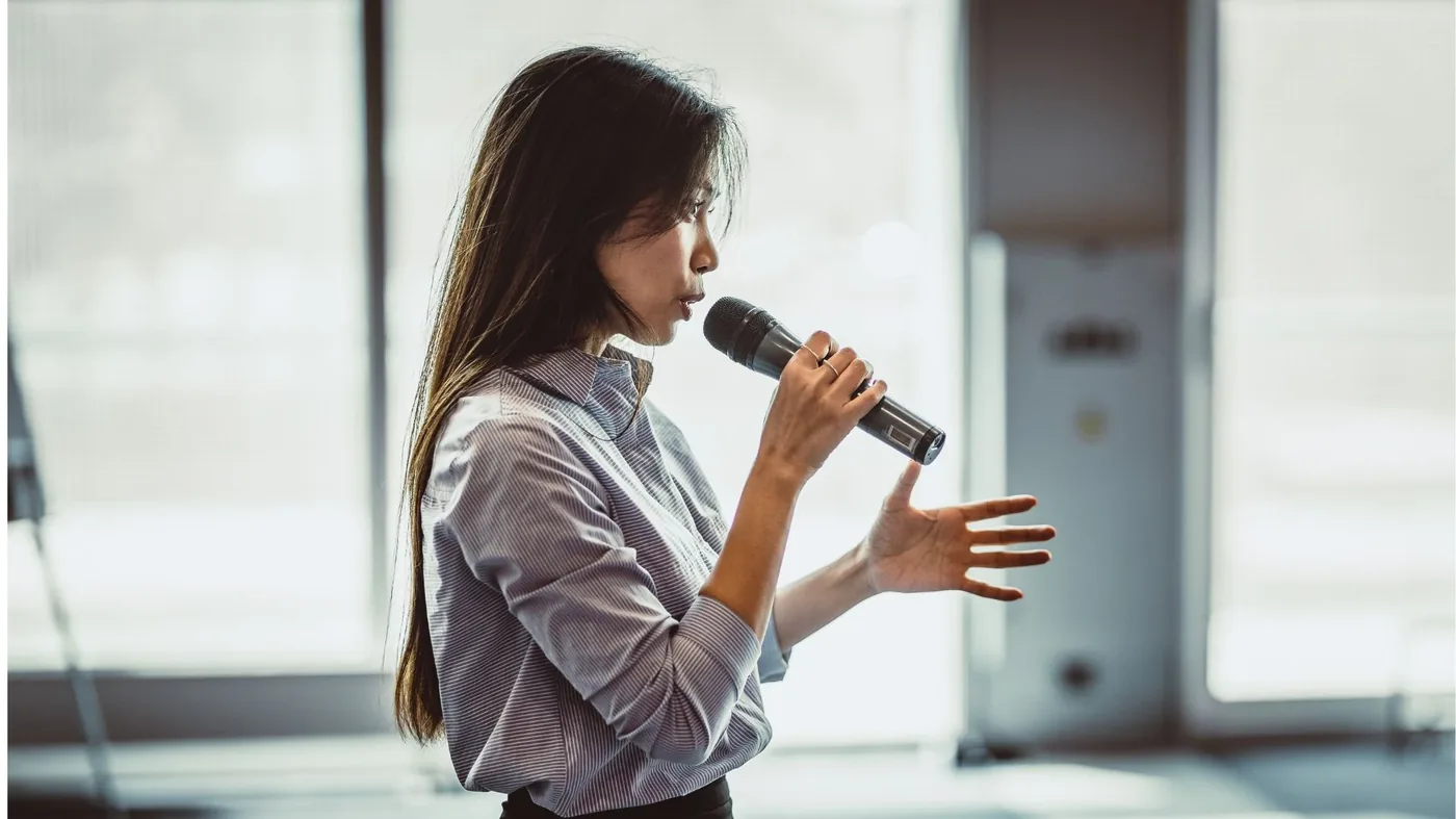 A speaker holding the room with calm presence and a mic — the lived-in craft of executive voice